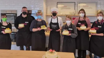 Sechs Personen präsentieren stolz ihre Kuchen in einer Küche.