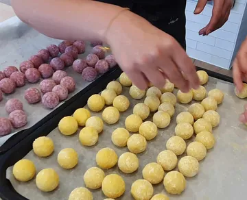 Hände formen bunte Kugeln auf einem Backblech.