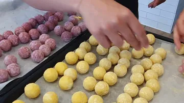 Hände formen bunte Kugeln aus Teig auf einem Blech.