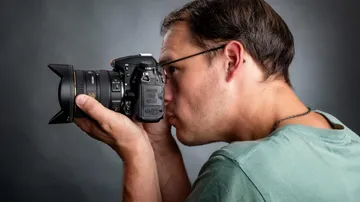 Ein Fotograf hält eine Kamera und fokussiert ein Motiv.