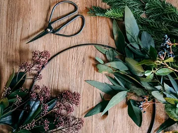 Green foliage and blossoms frame a wreath of wire on wood.
