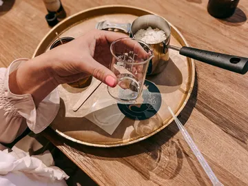 Hand holds a measuring glass over a golden plate.