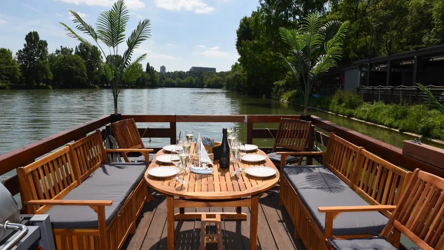 Holztisch mit Stühlen, gedeckt, am Fluss im Freien.