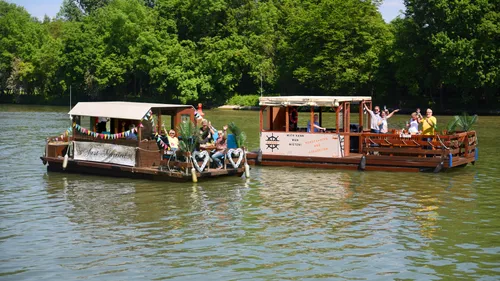 Two boats sail on a quiet river, people are partying.