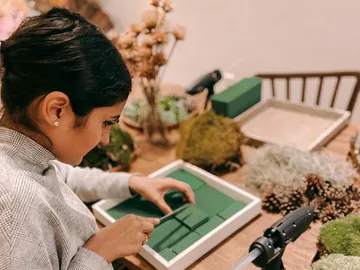 Frau arrangiert grüne Blumensteckschaumplatten auf einem Tisch.