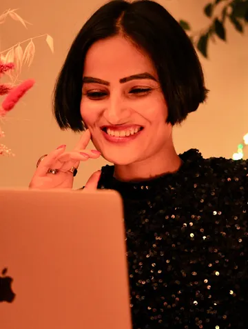 A laughing woman looks thoughtfully at a laptop.