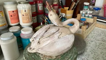 A swan sculpture stands on a table in a studio.