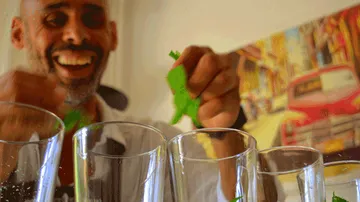 Bartender adds fresh ingredients into glasses in front of him.