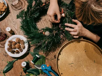 Person decorates a wreath on a wooden table.