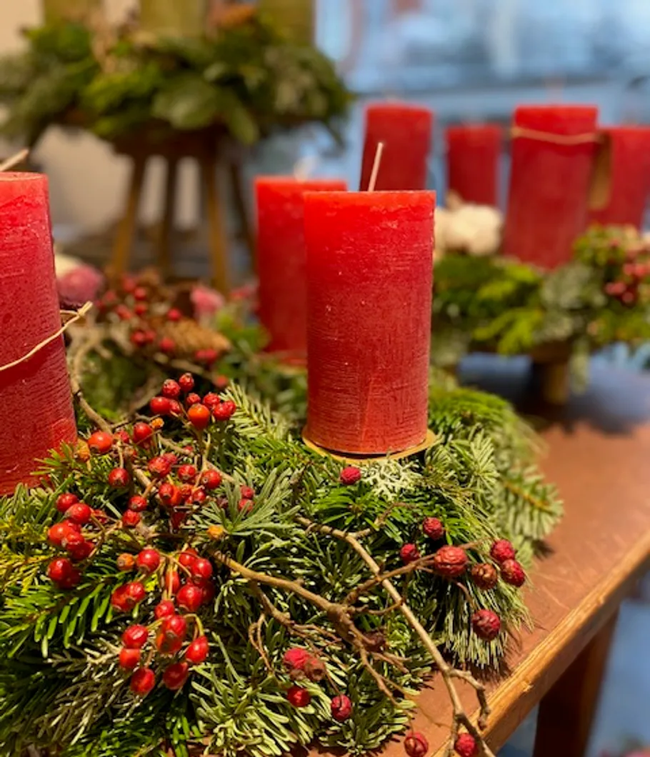 Rote Kerzen stehen auf einer grünen Adventskranzdekoration.