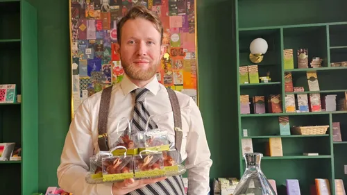 Mann hält Pralinenschachteln in einem Geschäft mit Bücherregalen.