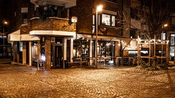 A restaurant is located on an illuminated, slightly busy street.