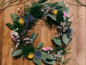 Blumenkranz liegt auf Holzoberfläche, dekorativ und farbenfroh.