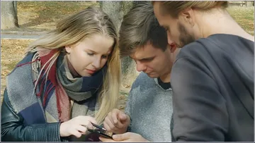 Drei junge Erwachsene schauen gemeinsam auf ein Smartphone.