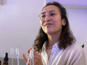 Young woman smiling, sitting in front of pipettes in a room.
