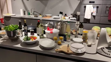 Küchentisch mit vielen Kochutensilien und frischen Zutaten.