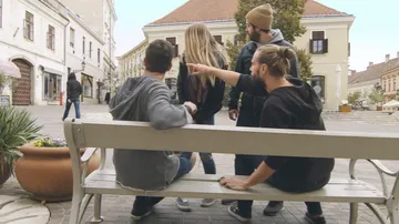 Vier Menschen stehen um eine Bank und zeigen auf etwas.