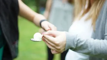One hand hands a spoon with a scoop of ice cream.