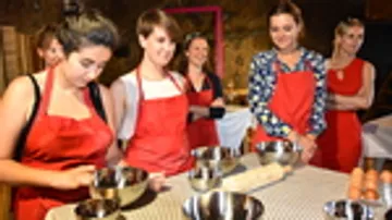 Frauen in roten Schürzen bereiten Essen in einer Küche vor.