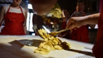 Dough is rolled out on a table surface, surrounded by people.