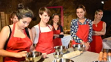 Women in red aprons cook together in a kitchen.