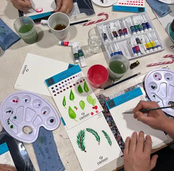 People paint with watercolors on paper, surrounded by painting supplies, water cups and tea cups. Creative atmosphere.