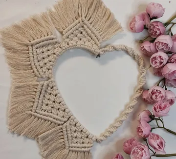 Macrame heart decorated with pink artificial flowers next to it