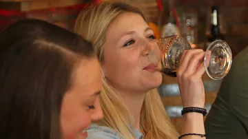 Frau trinkt aus einem Glas in einer geselligen Umgebung.