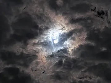 Bright sun shimmers through dark, cloudy skies.