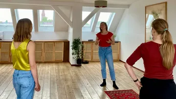 Drei Frauen kommunizieren in einem hellen Raum mit Holzfußboden.