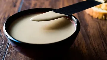 Schüssel mit cremiger Paste und Messer darauf. Holzuntergrund.