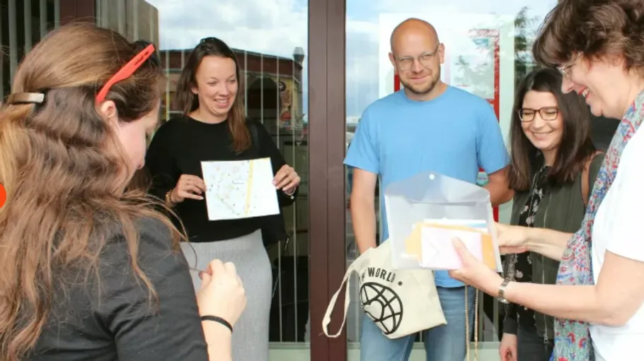 Group of people stand smiling at the entrance, holding cards and gifts.