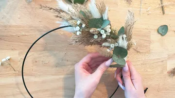 Hands arranging dried flowers on a wooden surface.