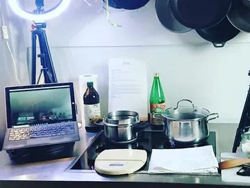 Laptop zeigt Video, Töpfe auf dem Kochfeld, Küche vorbereitet.