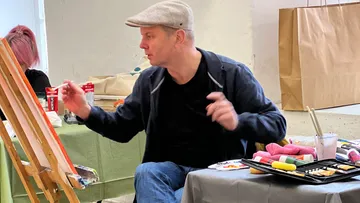 Ein Mann malt an einer Leinwand in einem Atelier.