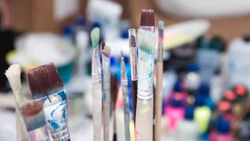 Brushes stand in a chaotic creative environment.