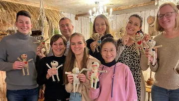 Group of people showing handmade dolls in a cozy room.