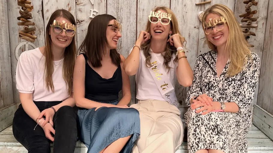 Four women sit laughing and wear sturdy glasses.