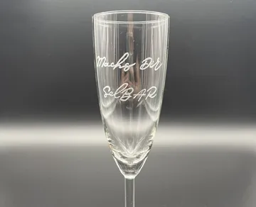 Glass with engraved text, presented against a dark background.