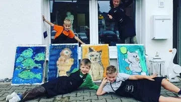 Four children pose in front of painted pictures outside.