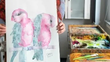 Zwei rosa Vögel werden von einer Person gehalten, umgeben von Farben.