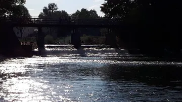River flows under a bridge in sunlight.