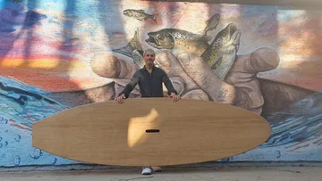 Mann hält ein großes Holzbrett vor einem Wandgemälde.