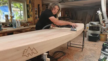 Ein Mann schleift ein Holzbrett in einer Werkstatt.