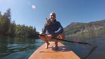 Mann paddelt auf einem Brett im stillen Gewässer.