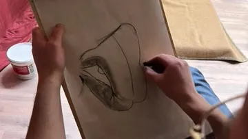 A hand draws a sketch on paper in a room.