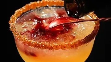 Cocktail wird mit Sirup aus Flasche verziert, dunkler Hintergrund.