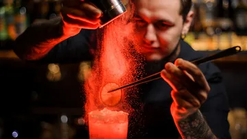 Barkeeper mischt Cocktail mit rotem Pulver in Bar.