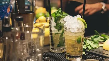Two cocktails with mint and ice are served at a bar.