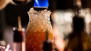 A glass is flambed over a cocktail with flames.